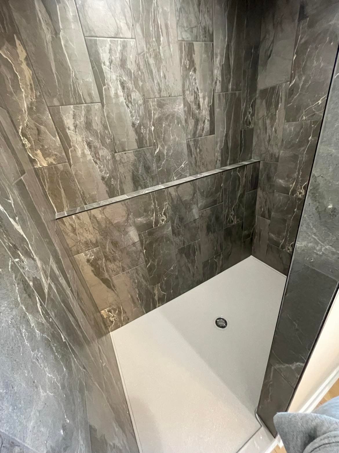 A bathroom with a walk in shower and a marble wall.