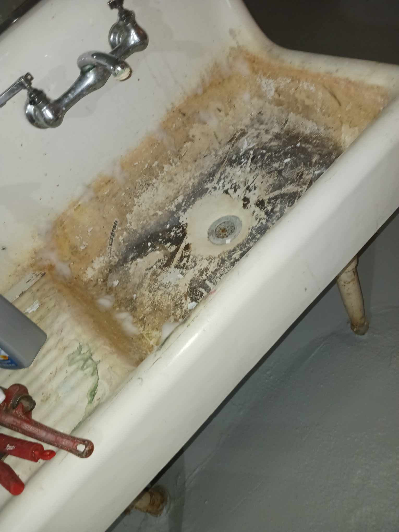 A dirty sink with a faucet and wrenches on the floor.