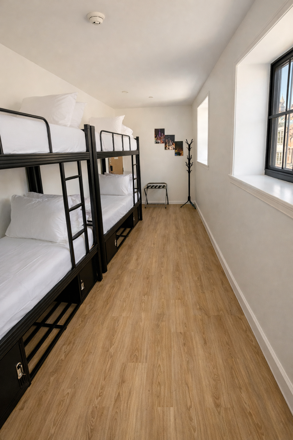 A bedroom with two black metal bunk beds, white bedding, wood-look flooring, and a large window along a white wall.
