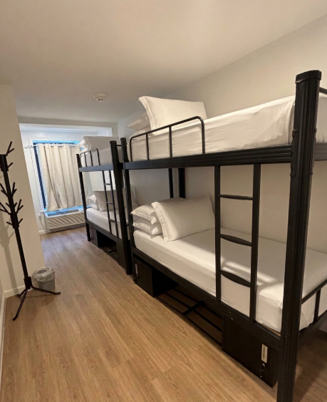 Two bunk beds with white bedding in a bright, modern room with light wood flooring and a coat rack.