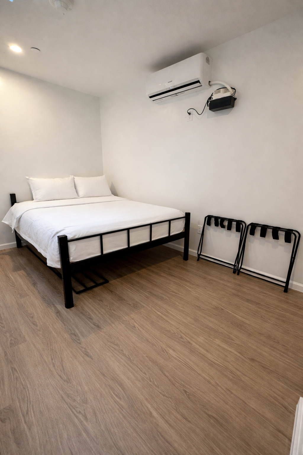 Hotel bedroom: bed, small table with laptop, sofa, and full-length mirror reflecting the room. Wooden floor.