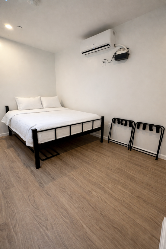 Hotel bedroom: bed, small table with laptop, sofa, and full-length mirror reflecting the room. Wooden floor.