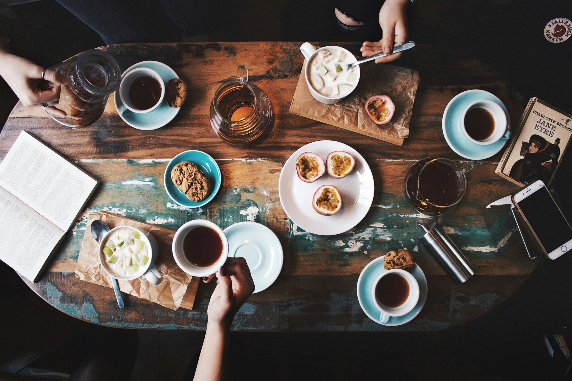 People at a wooden table enjoying coffee and treats, including passion fruit and cookies.