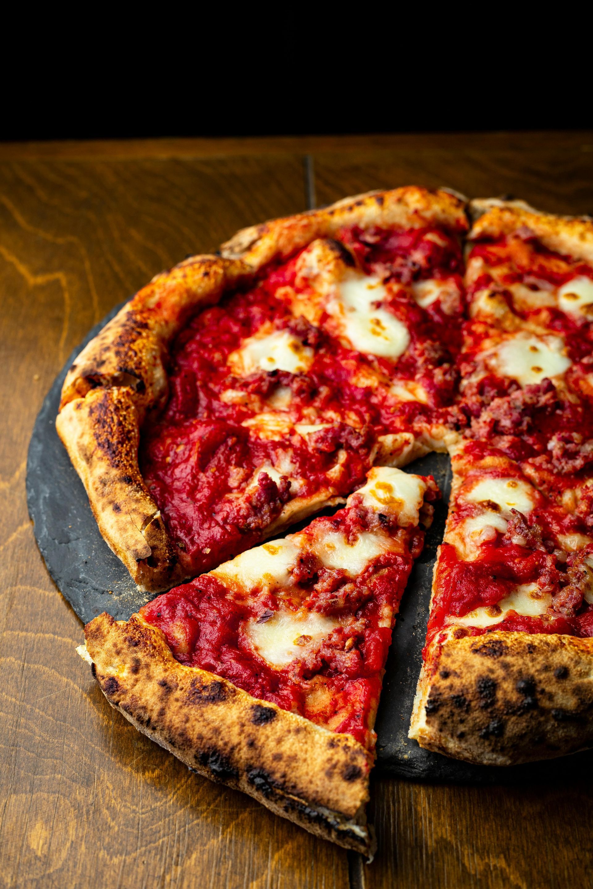 Pizza with tomato sauce, mozzarella, and browned crust on a dark slate, wooden table.