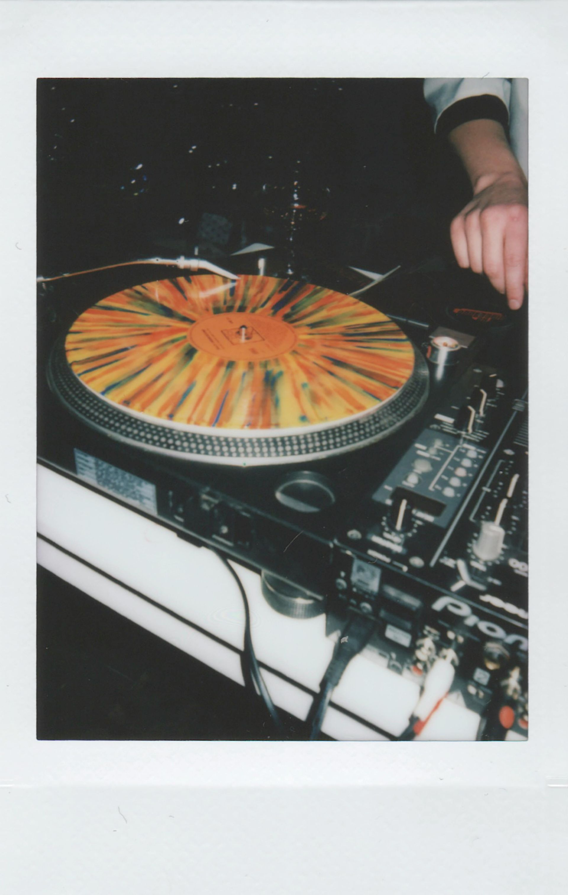 A hand adjusts a colorful, splattered vinyl record on a Pioneer DJ turntable.