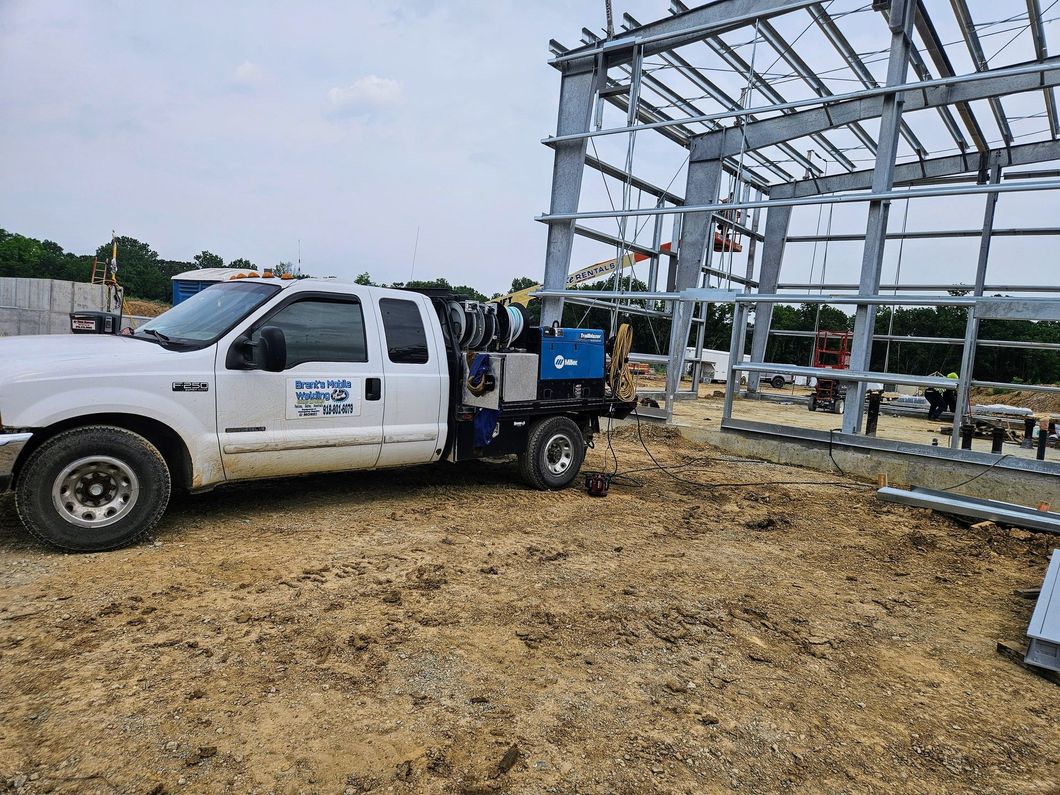 White work truck parked at a construction site with metal frame structure being built.