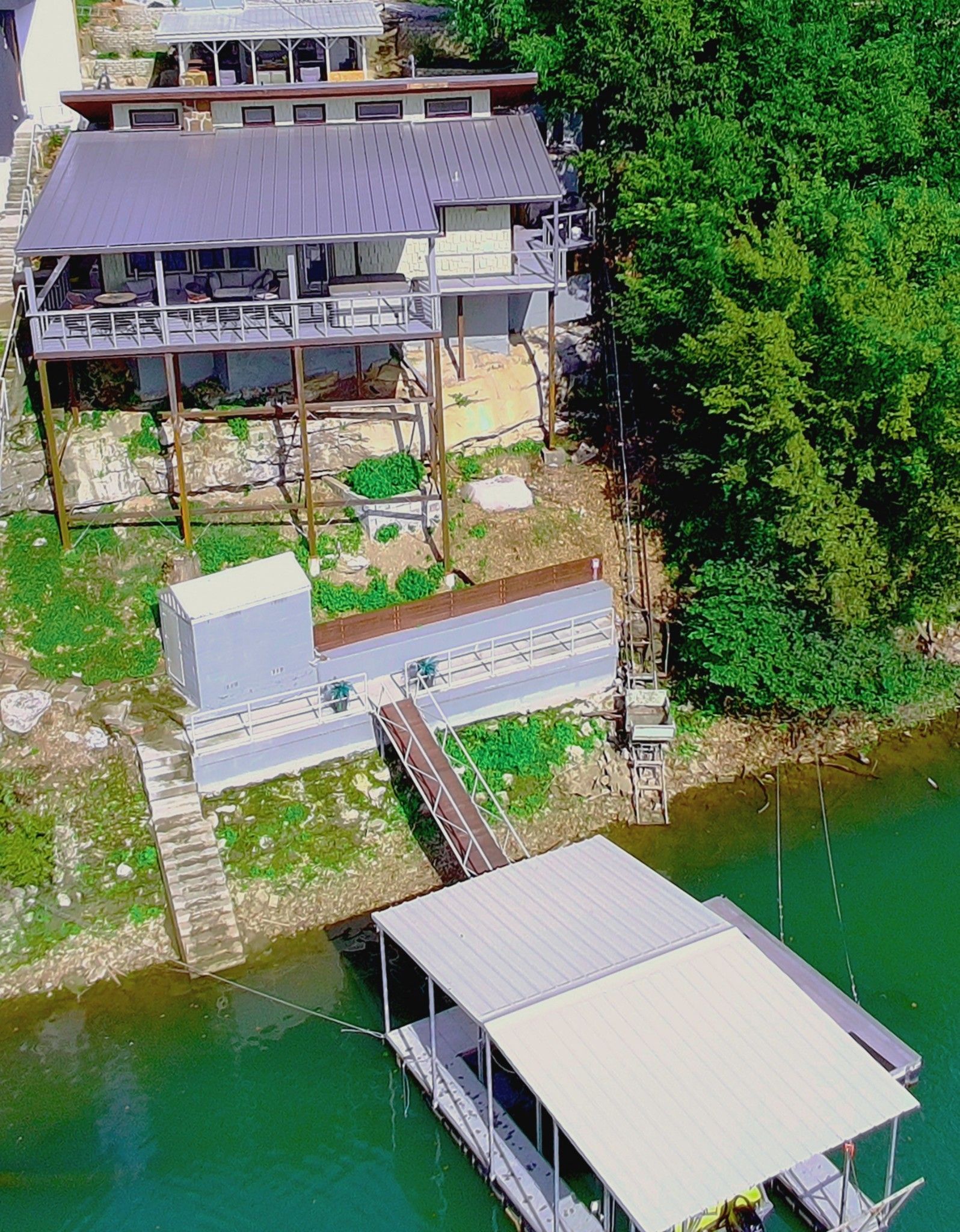 Houses on stilts on a lake, with a dock and boat. Green water and trees surround.
