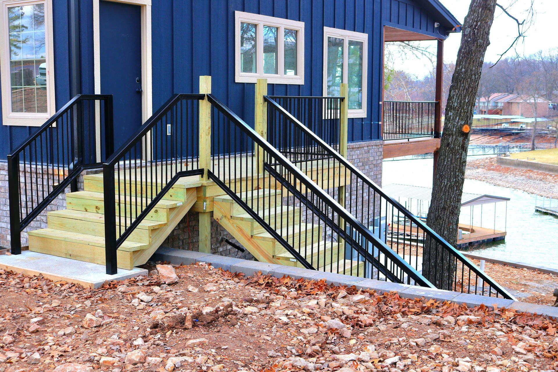 A blue house with wooden stairs and black railings leading up from a yard with brown soil.
