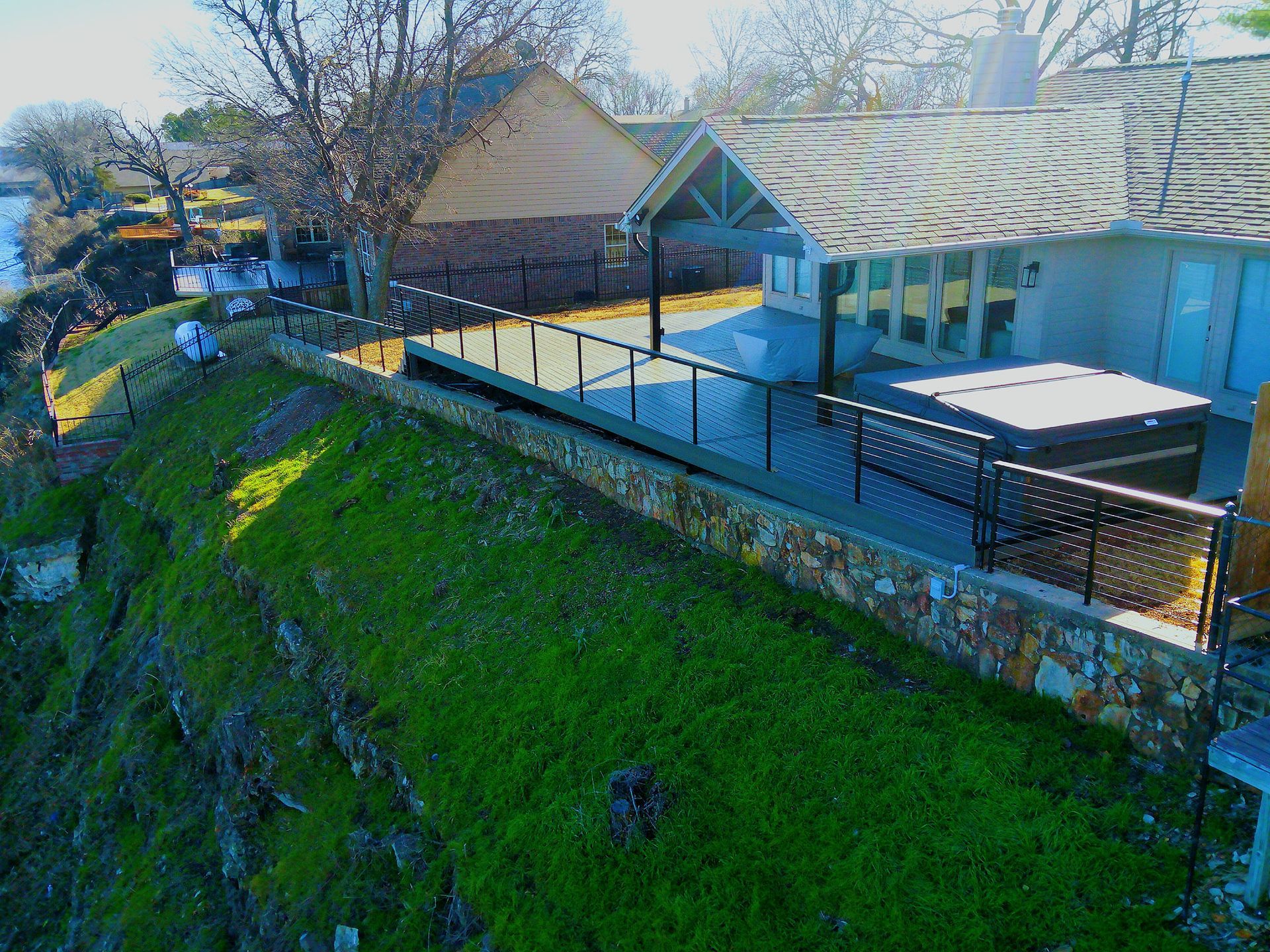 A house with a deck overlooking a body of water, hot tub, and a grassy hill.