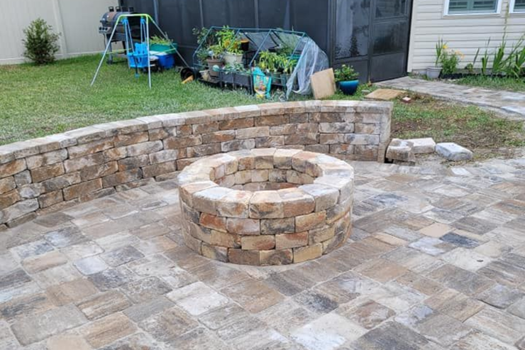 Stone patio with circular fire pit and curved retaining wall in a backyard