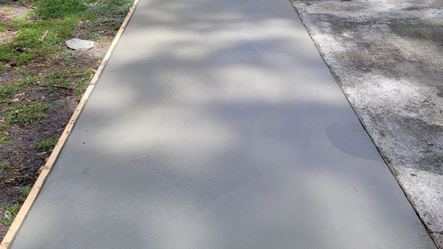 Concrete sidewalk bordered by grass and gravel in dappled sunlight