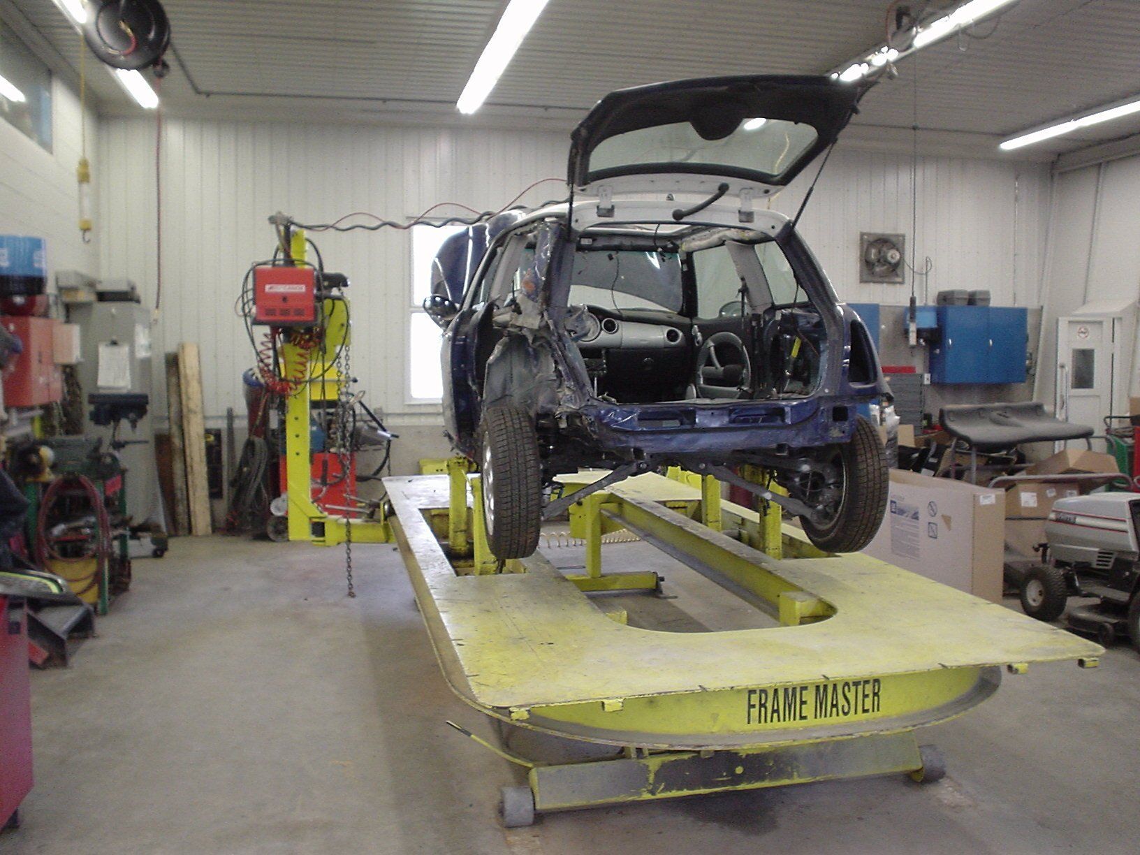 Une voiture bleue endommagée sur une machine à redresser les châssis dans un garage.