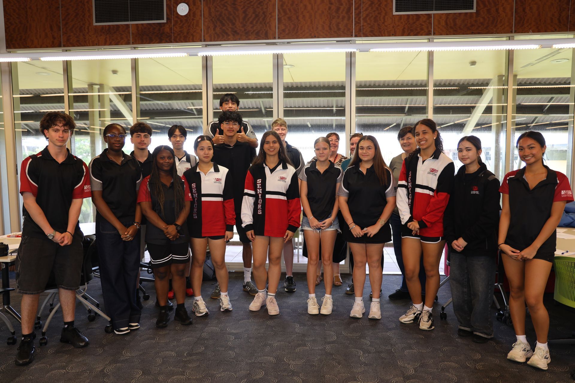 Group of people at a faculty event, smiling. Some wear black & red uniforms, others in dress clothes. Banners in background.