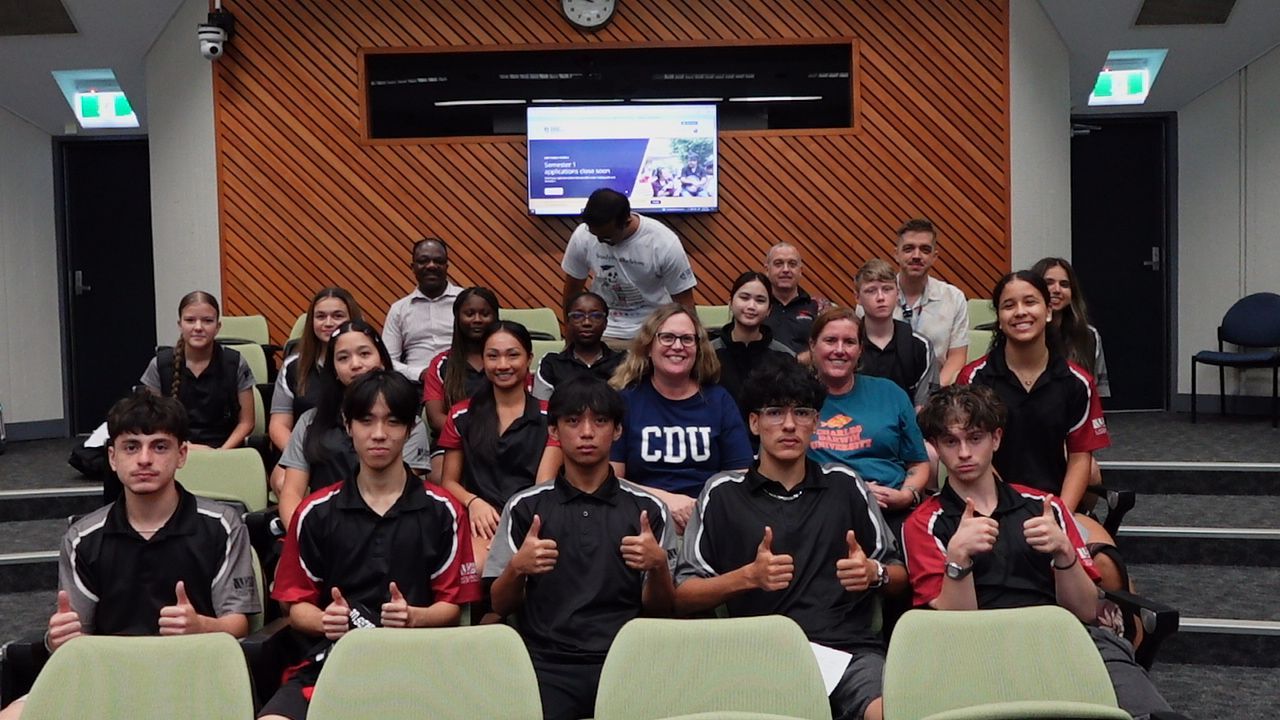 Group of students in sports attire at an event, posing with banner backdrop.