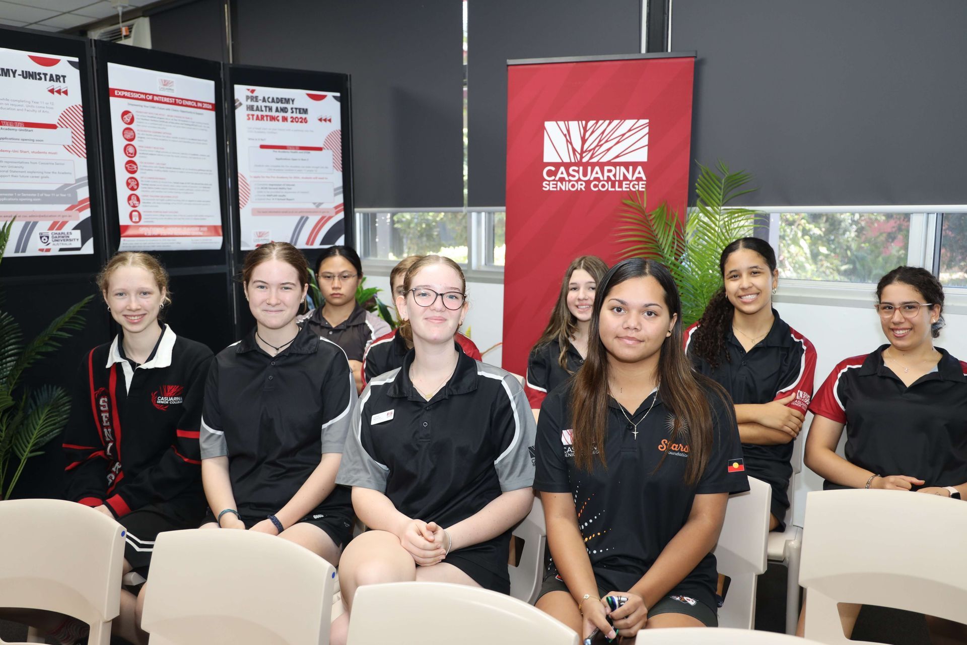 Group of students in sports attire at an event, posing with banner backdrop.