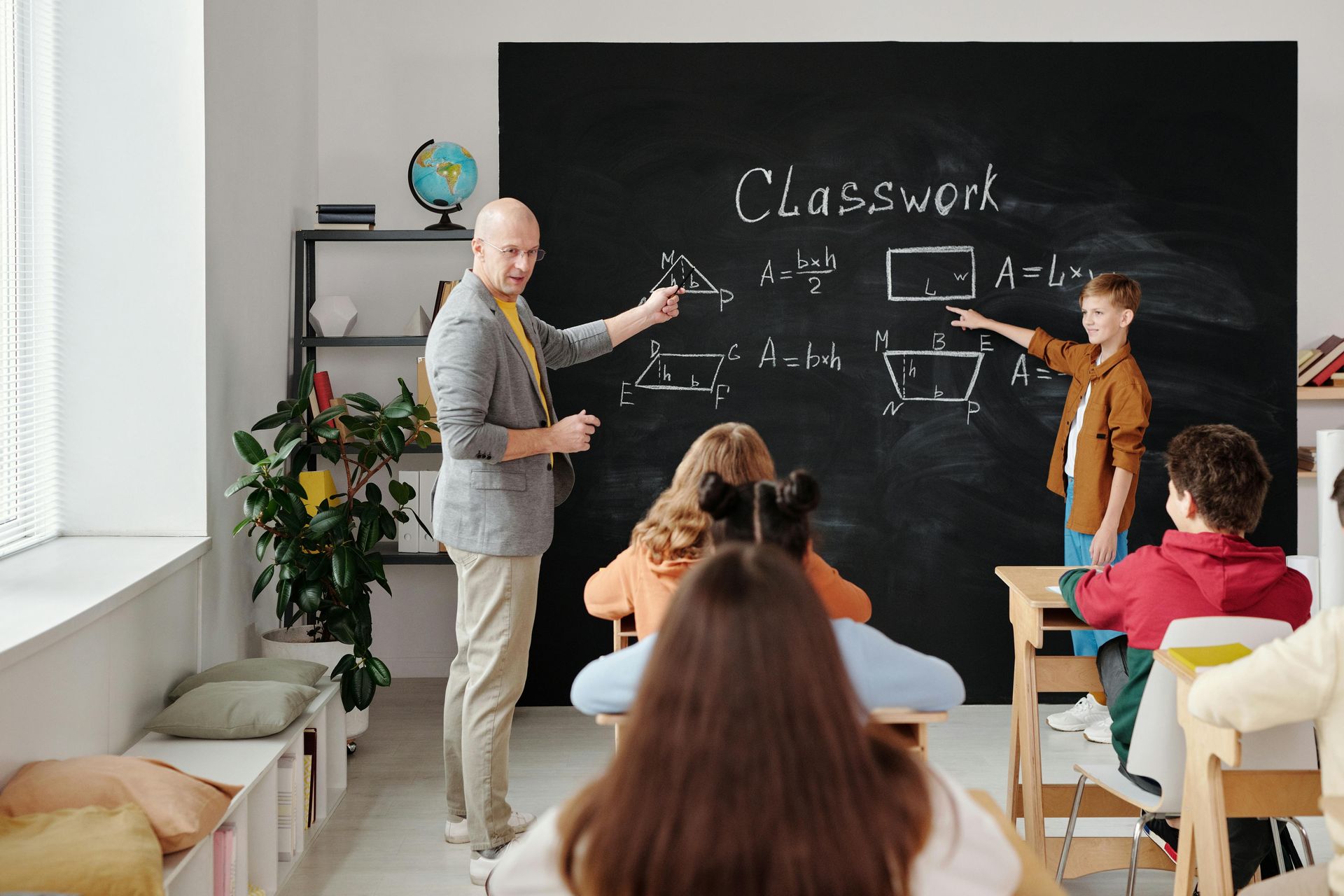 Teacher and student at chalkboard, explaining geometry shapes. Students in classroom setting.