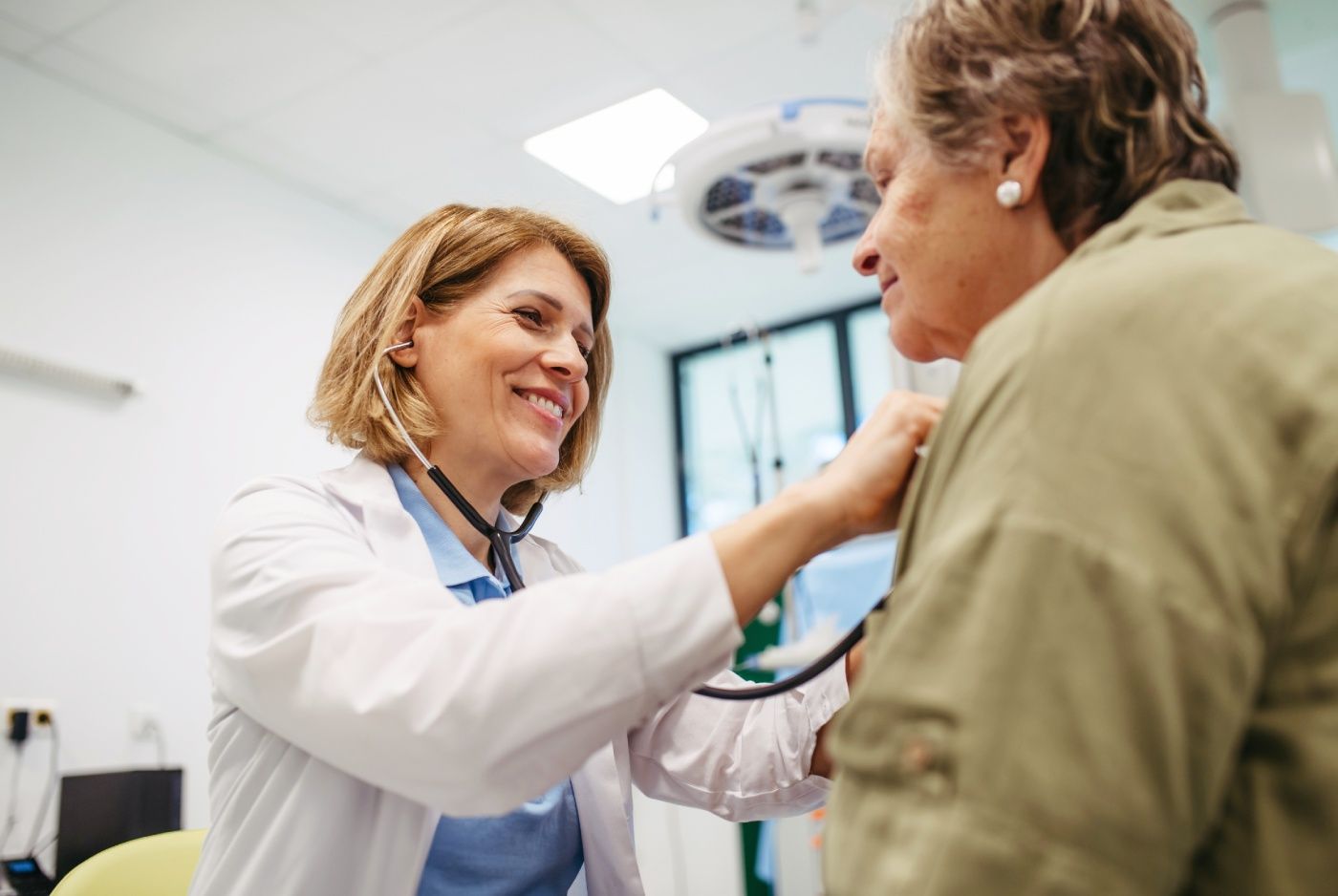Doctor using a stethoscope to examine a patient's chest in a medical office.