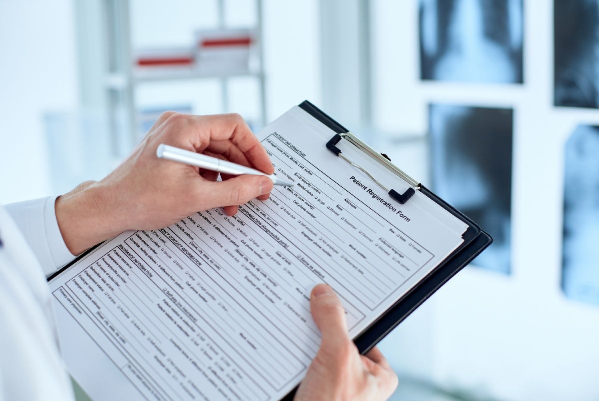Doctor writing on a medical form, with X-rays in the background.