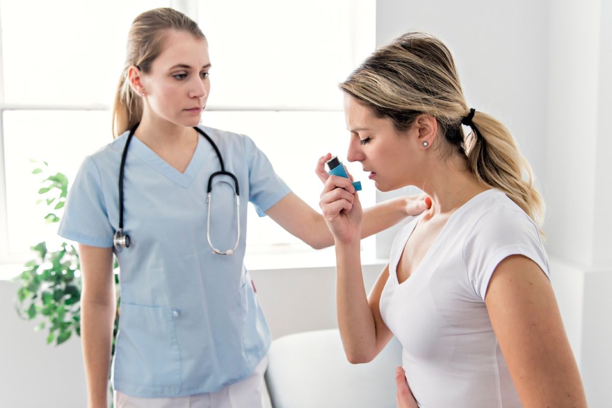 A nurse assists a patient using an inhaler indoors.