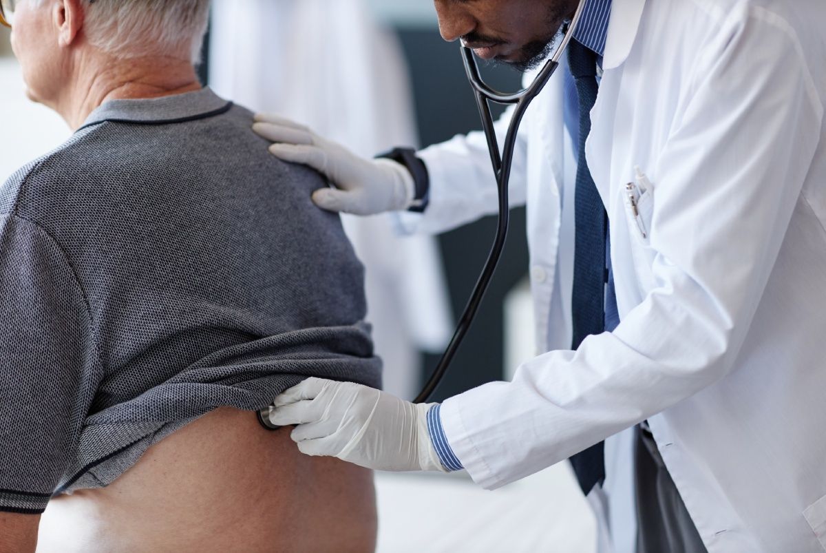 Doctor using a stethoscope to examine a patient's back in a medical setting.