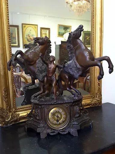 Un orologio con due cavalli e un uomo sopra è seduto su un tavolo davanti a uno specchio.