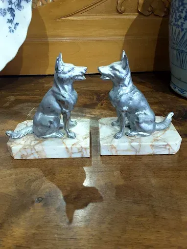 Una coppia di cani d'argento seduti su fermalibri di marmo su un tavolo di legno.