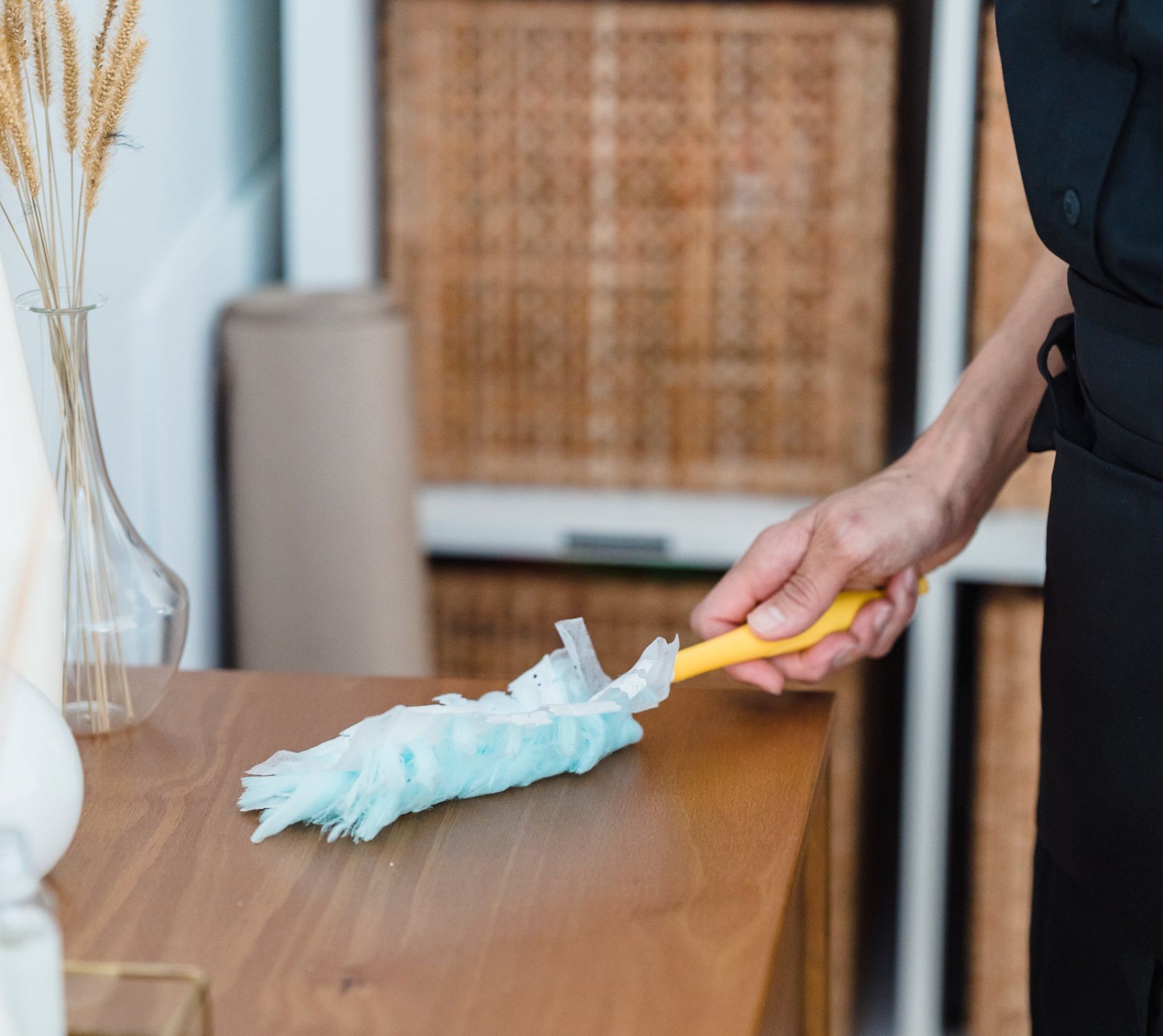 A person is cleaning a wooden table with a duster.