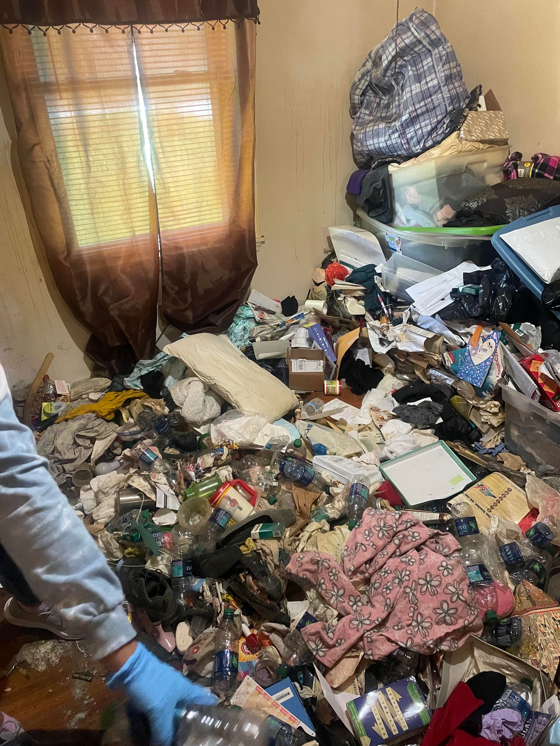 A person is standing in a room filled with lots of trash.