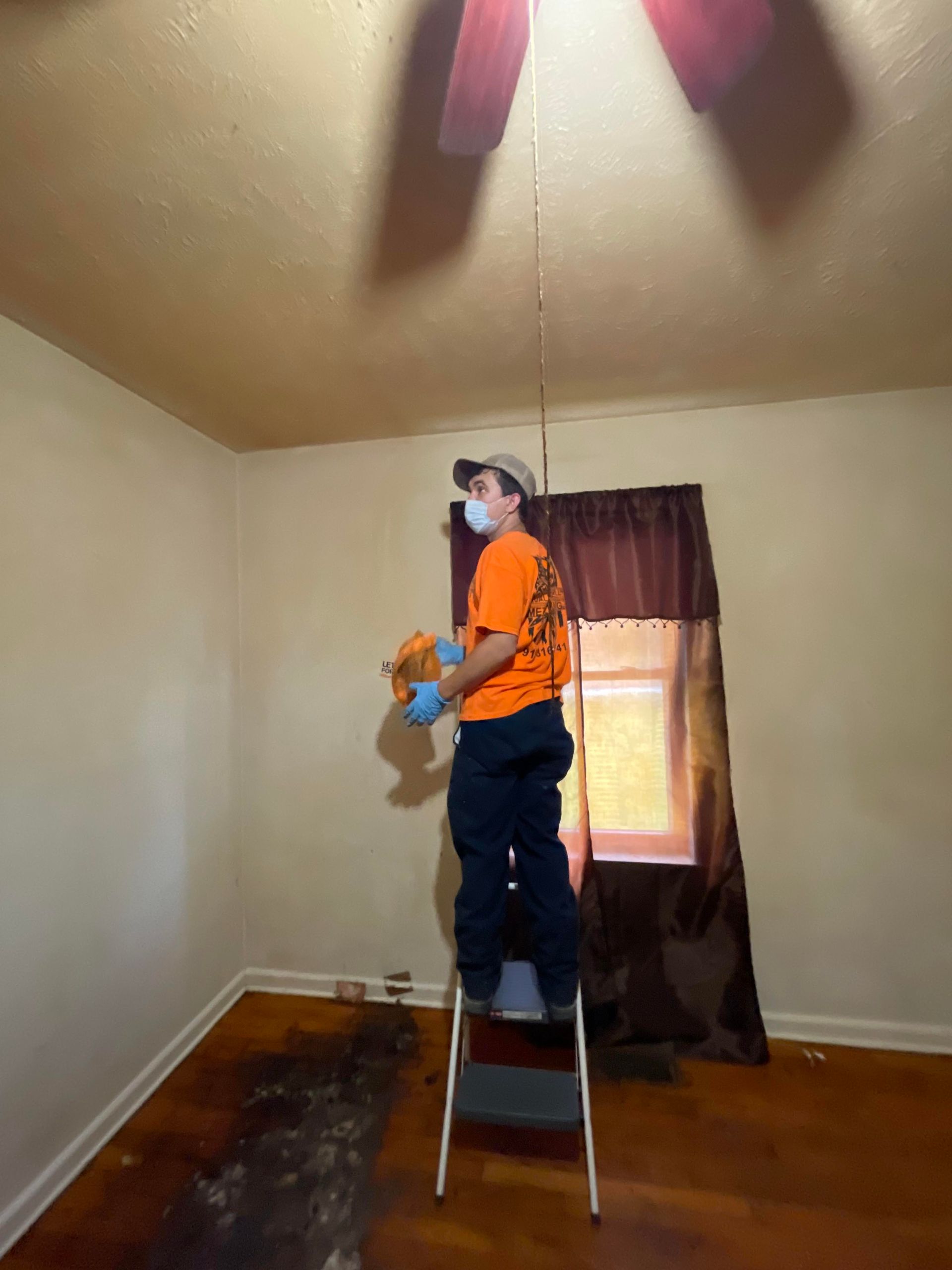 A man wearing a mask is standing on a ladder in a room