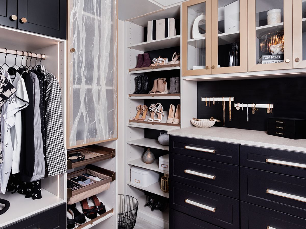 A black finish walk in closet filled with clothes , shoes , and jewelry.