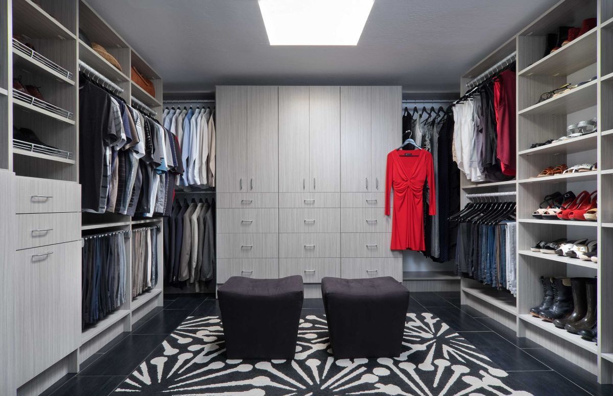 A large walk in closet with a red dress hanging on the wall.