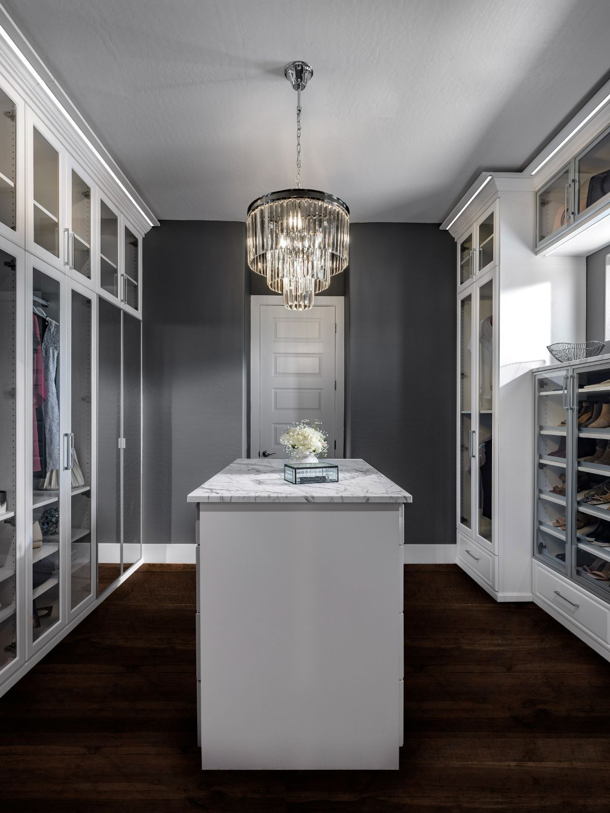 A walk in closet with a large island in the middle and a chandelier hanging from the ceiling.
