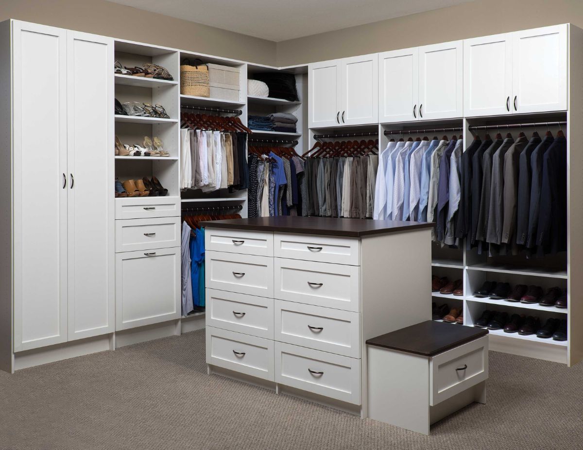 A walk in closet with white cabinets and drawers and a large island in the middle.
