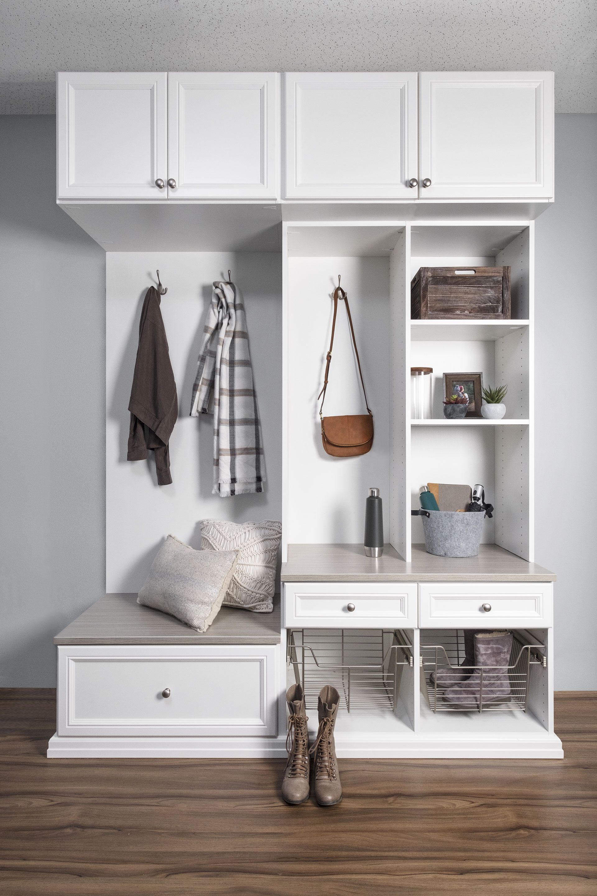 A mud room with white cabinets , shelves , a bench , and a pair of boots.