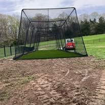 Black netting baseball batting cage on artificial turf, outside.