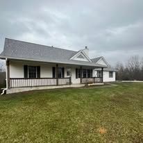 A one-story white house with a gray roof and a green lawn on a cloudy day.