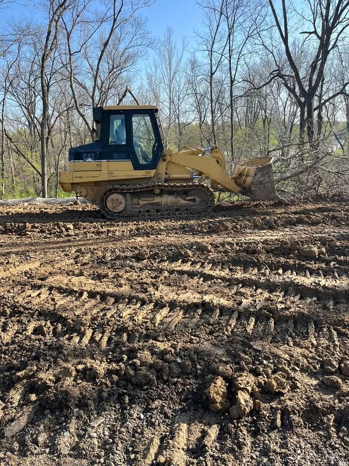 Yellow bulldozer on muddy ground, trees in background, sunny day.