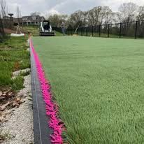 A lawn care machine on artificial turf with a bright pink edging.