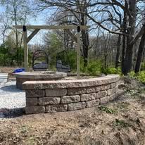 Stone fire pit with built-in seating, wooden swing set in outdoor setting.