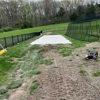 Dirt field with a white rectangular area, fencing, and a machine.
