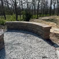 Stone retaining wall on a gravel bed, curving along a path, with trees in the background.