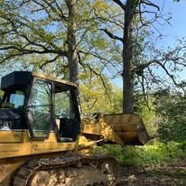 Yellow bulldozer working near trees in a natural setting.