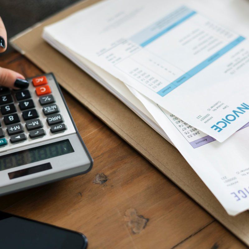 Person calculating with a calculator, with invoices and a phone on a wooden table.