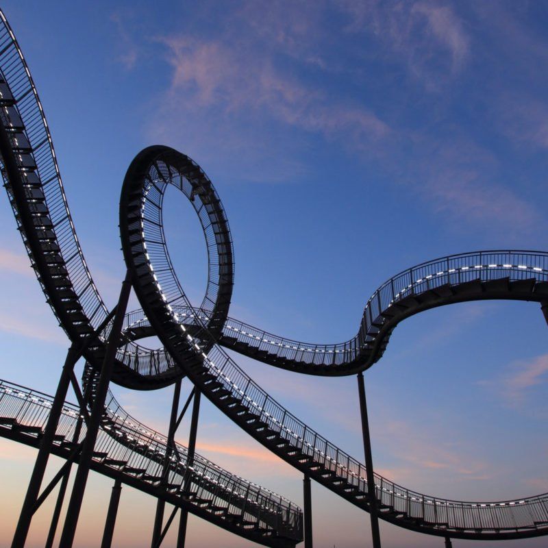 Metal roller coaster-like structure with loops and stairs against a dusky blue sky.
