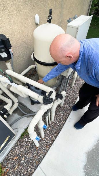 A man in a blue shirt is working on a pool filter.