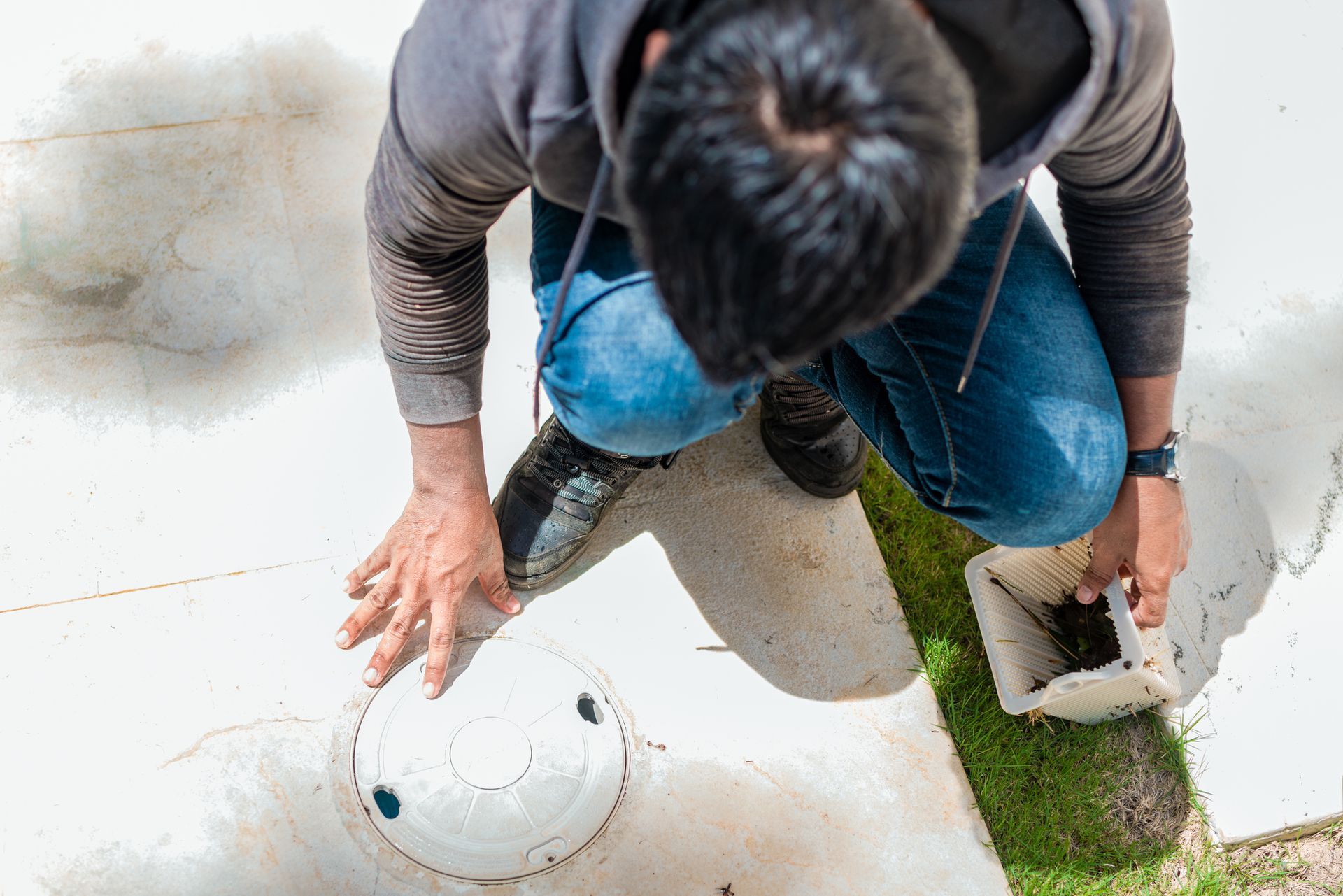 A man is kneeling down on the ground looking at a hole in the ground.