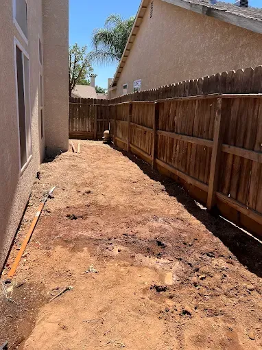 A dirt yard with a wooden fence and a house in the background.