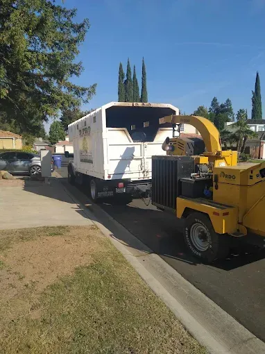 A white truck with a yellow chipper attached to it is parked on the side of the road.