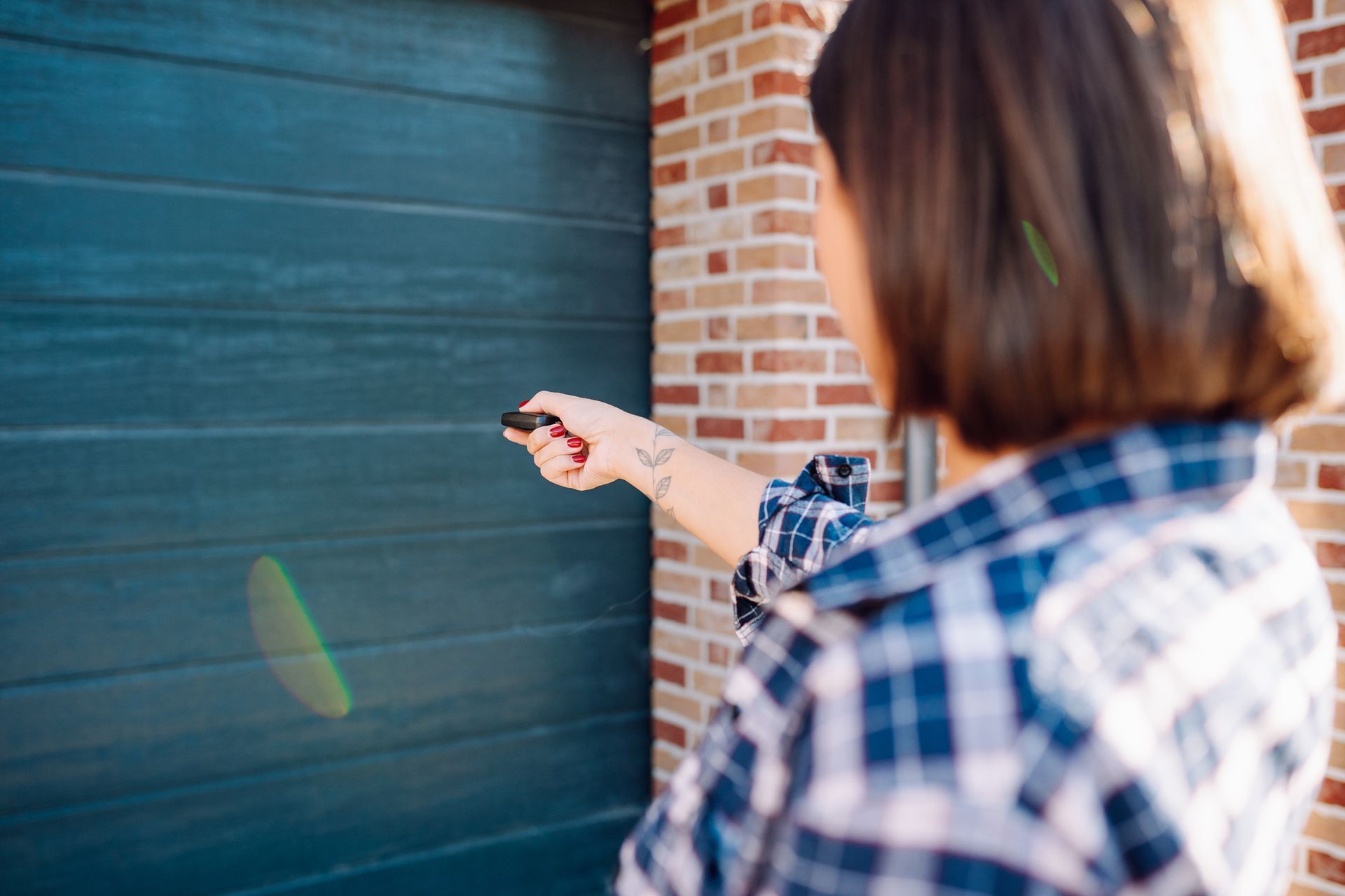 A woman extends her arm to open her garage’s door with a remote controller.