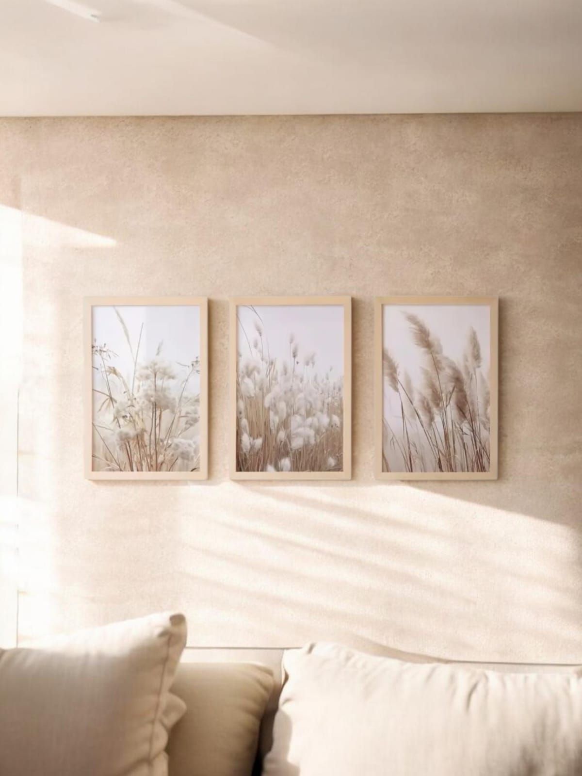 Pared minimalista de color beige en la sala de estar con tres láminas botánicas enmarcadas sobre un sofá color crema.